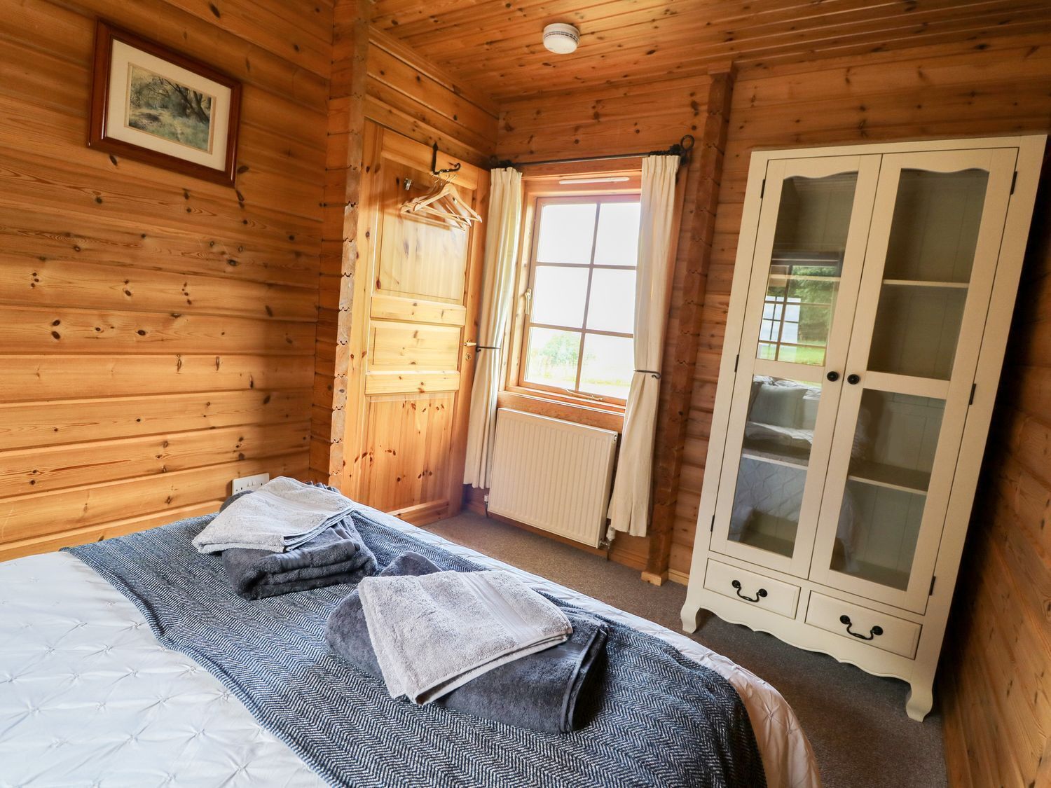 Una habitación de madera con una cama, un armario y una ventana.