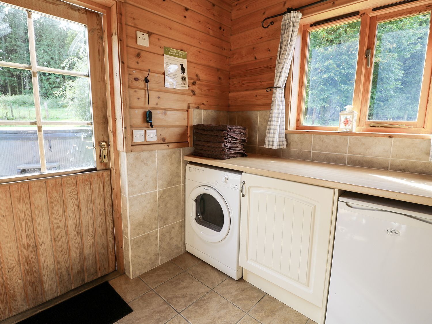 A small, wooden cabin with a washing machine, a drying rack, and a window with curtains.