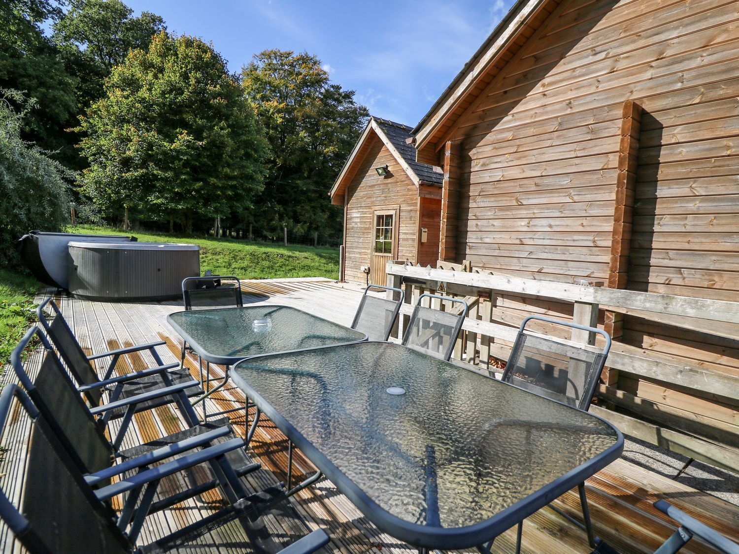 A wooden cabin with a glass table and chairs, a hot tub, and a deck.