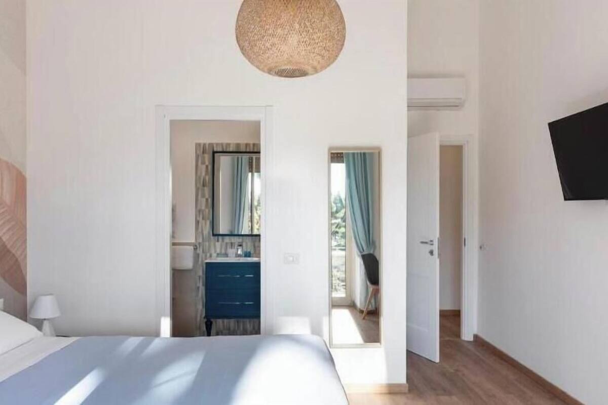 A bedroom with a bed, a dresser, a mirror, and a television on the wall.