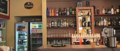 Zona de bar con estantes llenos de botellas de licores, un refrigerador con bebidas y una máquina de café.