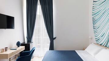 A hotel room with a bed, a desk with a chair, a television, and a window with curtains.
