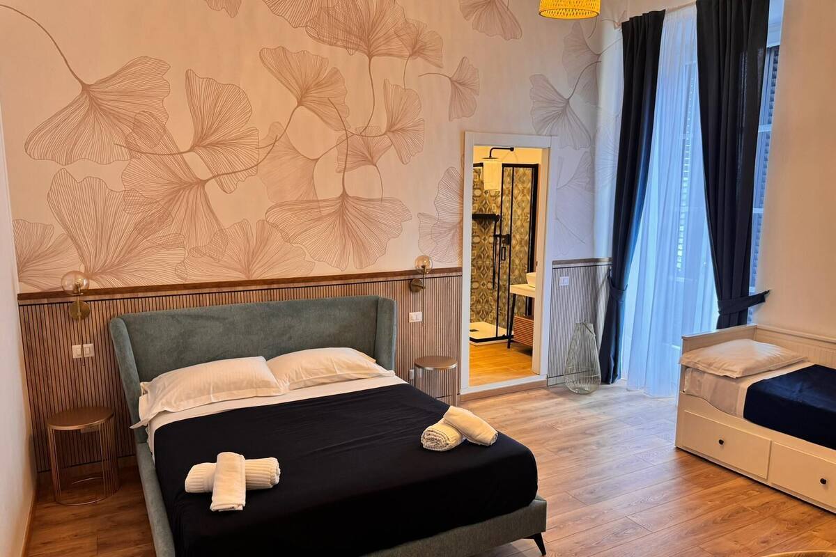 A modern bedroom with a bed, a bedside table, a chair, and a bathroom visible through an open door.