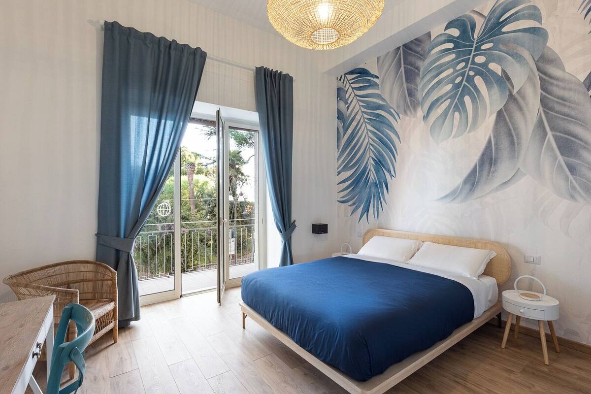 A bedroom with a bed, a chair, a nightstand, and a large window with curtains.