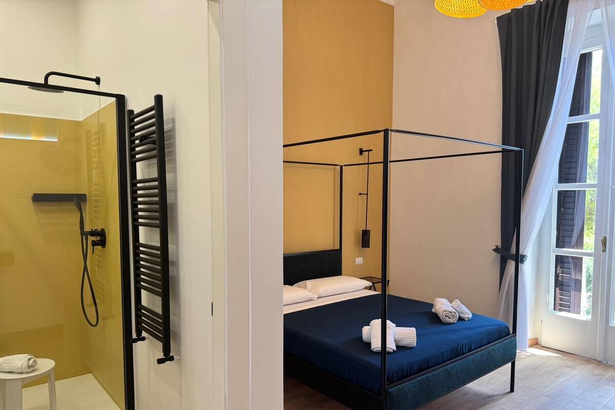 A room with a four-poster bed, a shower area, and a small table with towels.