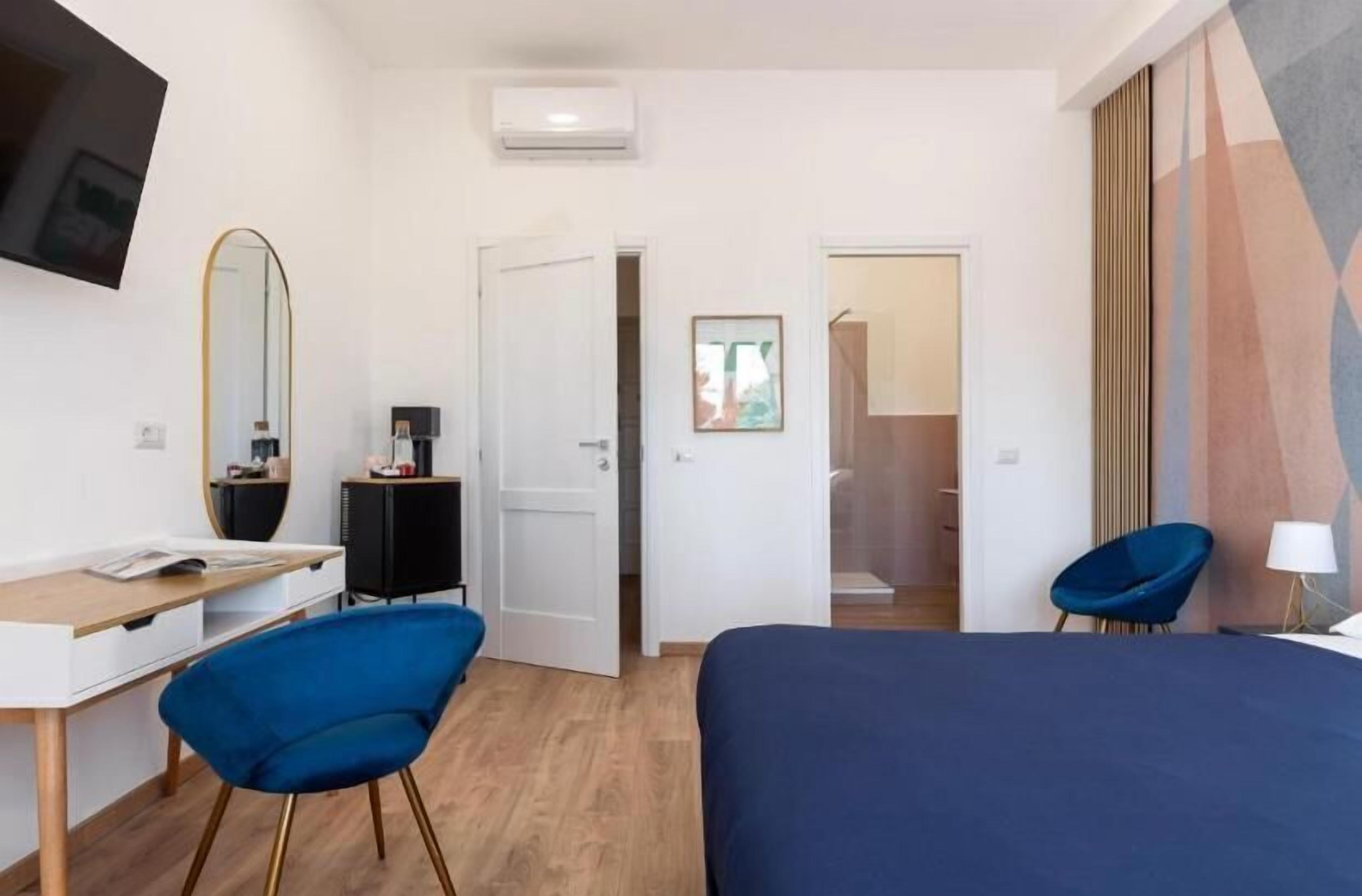 A hotel room with a bed, a desk, a chair, a TV, and a door leading to another room.