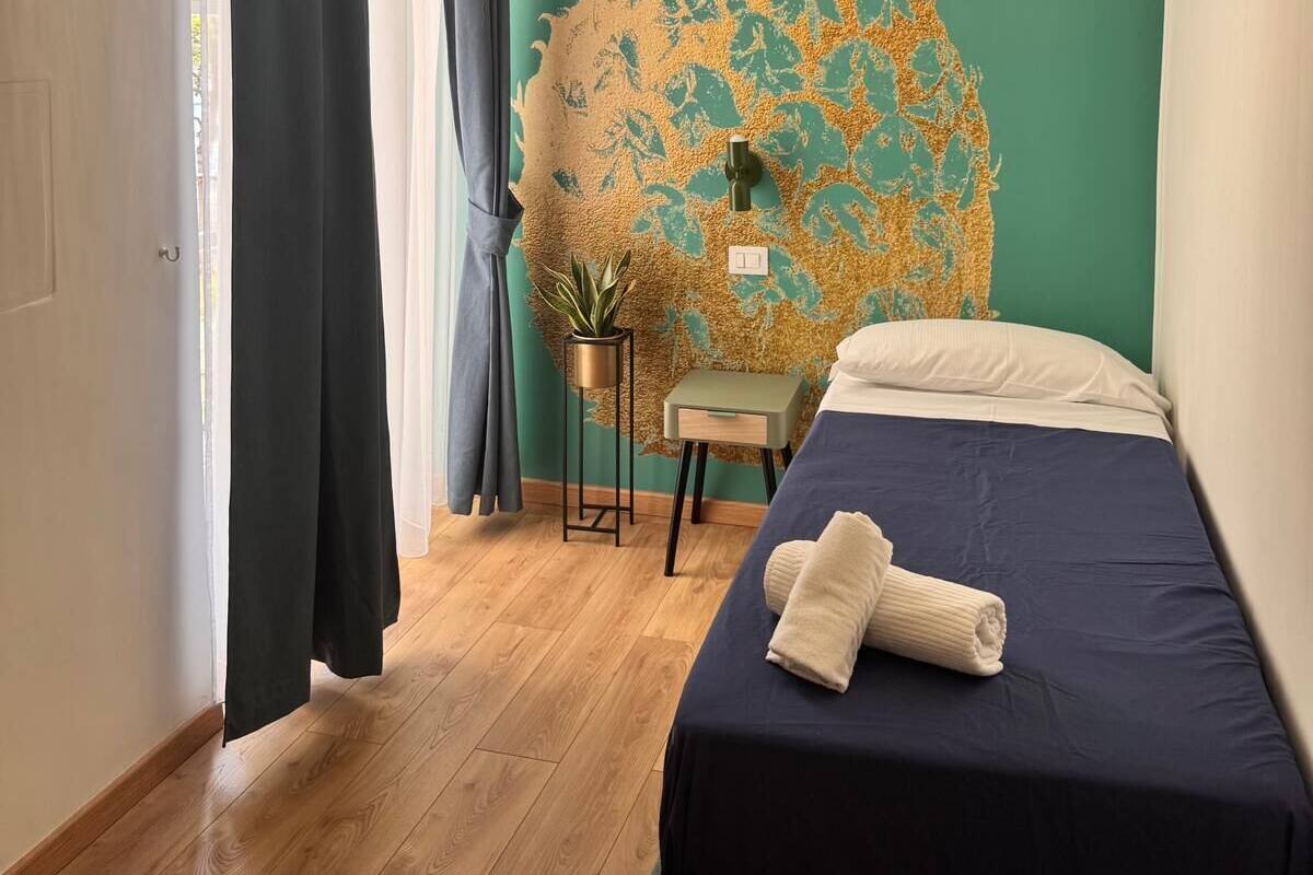A bedroom with a bed, a wall mural, a hanging light fixture, and a window with curtains.