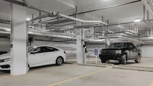 A parking garage with multiple levels, concrete pillars, and overhead pipes.