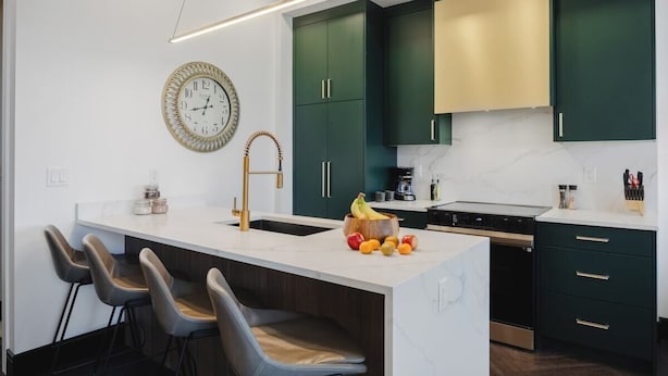 A modern kitchen with a central island, bar stools, a sink, and green cabinets.