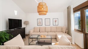 A modern living room with a sectional sofa, a glass coffee table, a television on a dark cabinet, and a large window with curtains. - Villa Mima Pool Retreat (Lovreć)