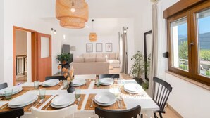 A dining area with a table set for four, a hanging orange pendant light, and a view of the outdoors through a large window. - Villa Mima Pool Retreat (Lovreć)