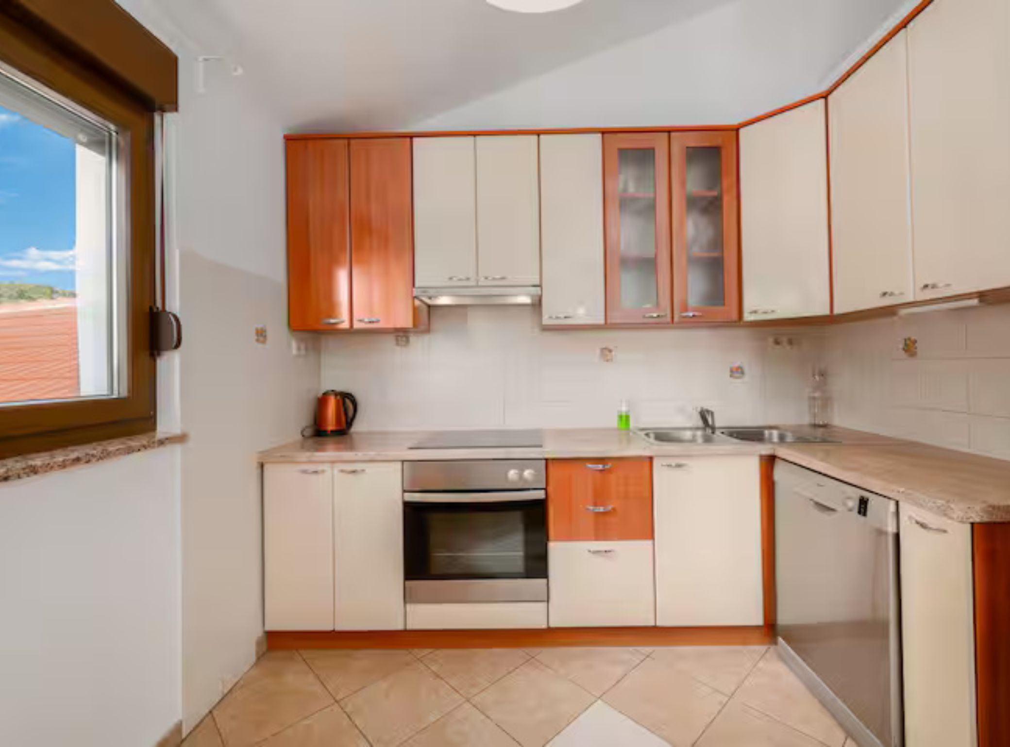 A compact kitchen with white and wooden cabinets, a stainless steel oven, and a window with a view of the outdoors.