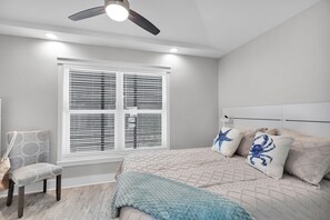 Un dormitorio con cama, una silla, una ventana con persianas y un ventilador de techo.