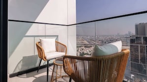 Ein Balkon mit Korbstühlen und einer Glasböden, mit Blick auf die Stadt.