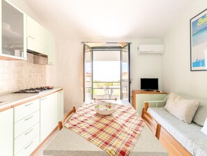 A compact room with a kitchenette, a dining table with a plaid tablecloth, a sofa, and a TV. - 150 Meters From the Sea, 2 Swimming Pools (Valledoria)