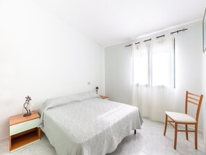 A small, clean room with a bed, a nightstand, a chair, and a window with curtains. - 150 Meters From the Sea, 2 Swimming Pools (Valledoria)