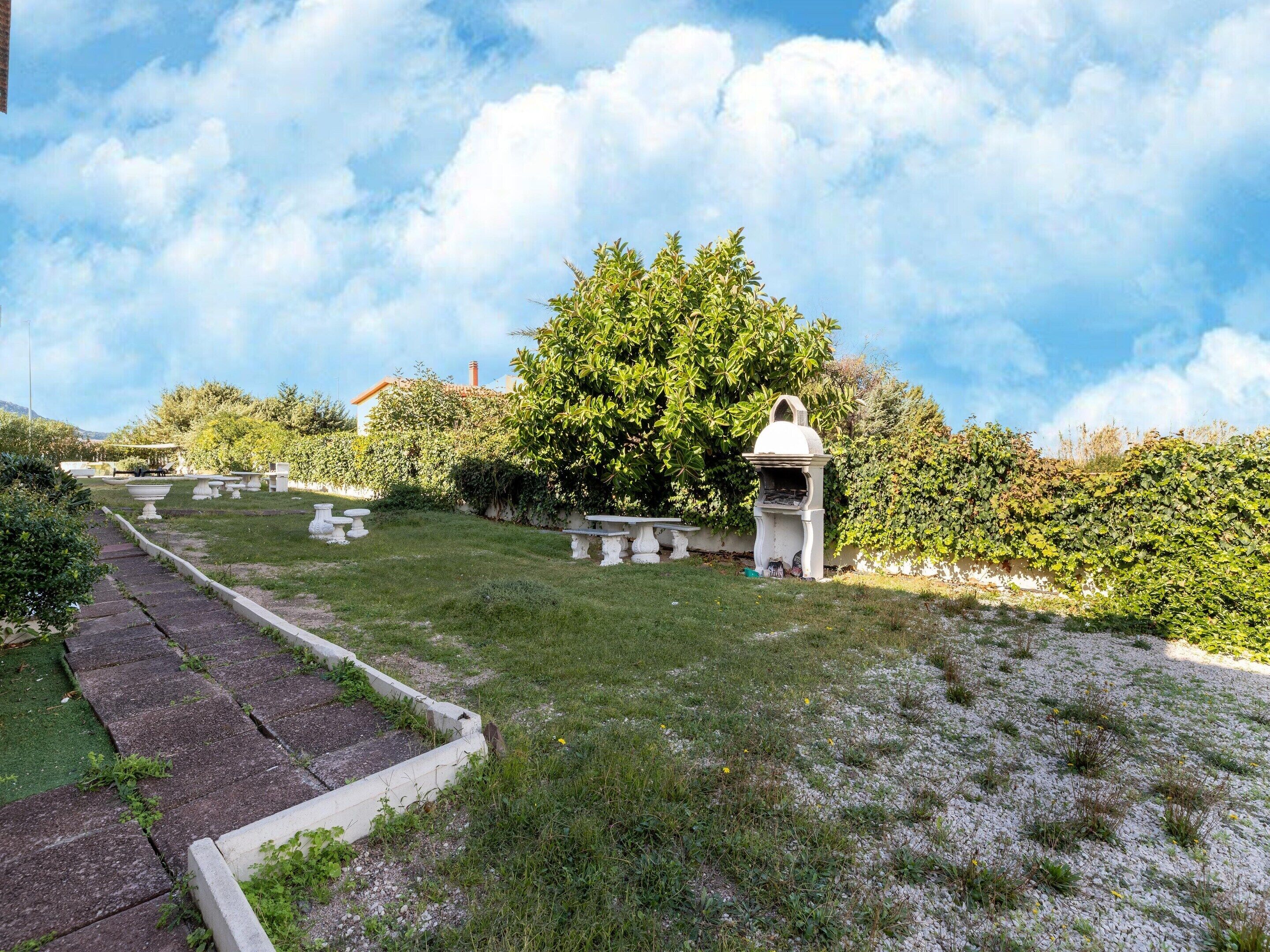 A garden with a white gazebo, a paved pathway, and a large tree.