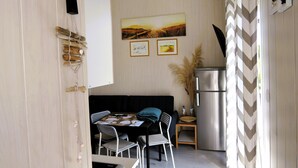 A compact kitchen with a dining area, featuring a black sofa, a small table, and a refrigerator. - New Holiday Home for 5 People in Wiselka (gmina Wolin)