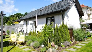 A modern house with a sloped roof, a small garden with various plants, and a signboard in the front yard. - New Holiday Home for 5 People in Wiselka (gmina Wolin)