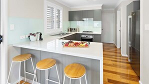 A modern kitchen with a central island, bar stools, a stainless steel refrigerator, and a window with blinds.