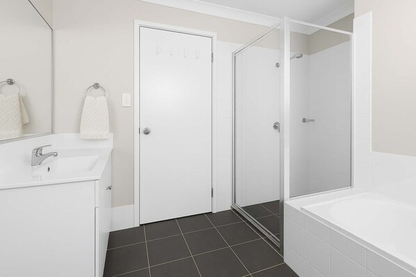 A modern bathroom with a white sink, a mirror, a shower enclosure, and a bathtub.