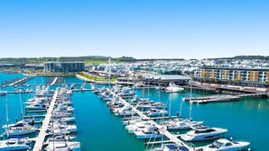 A marina with numerous boats docked, a large modern building, and a marina with a clear blue sky.