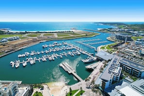 Ein Yachthafen mit zahlreichen Booten, ein großes Gebäude mit Solaranlage und freier Sicht auf den Ozean.