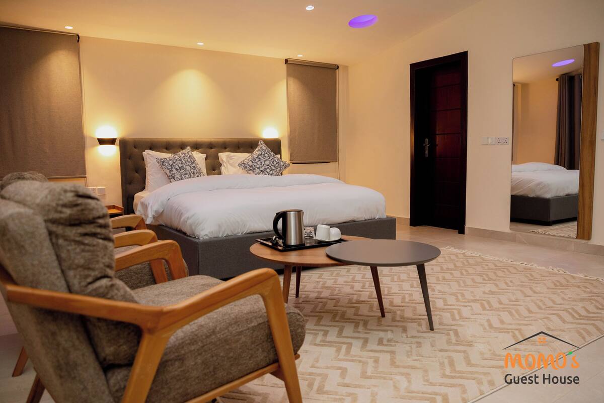 A hotel room with a large bed, two bedside tables, a coffee maker, and a seating area with chairs and a small table.