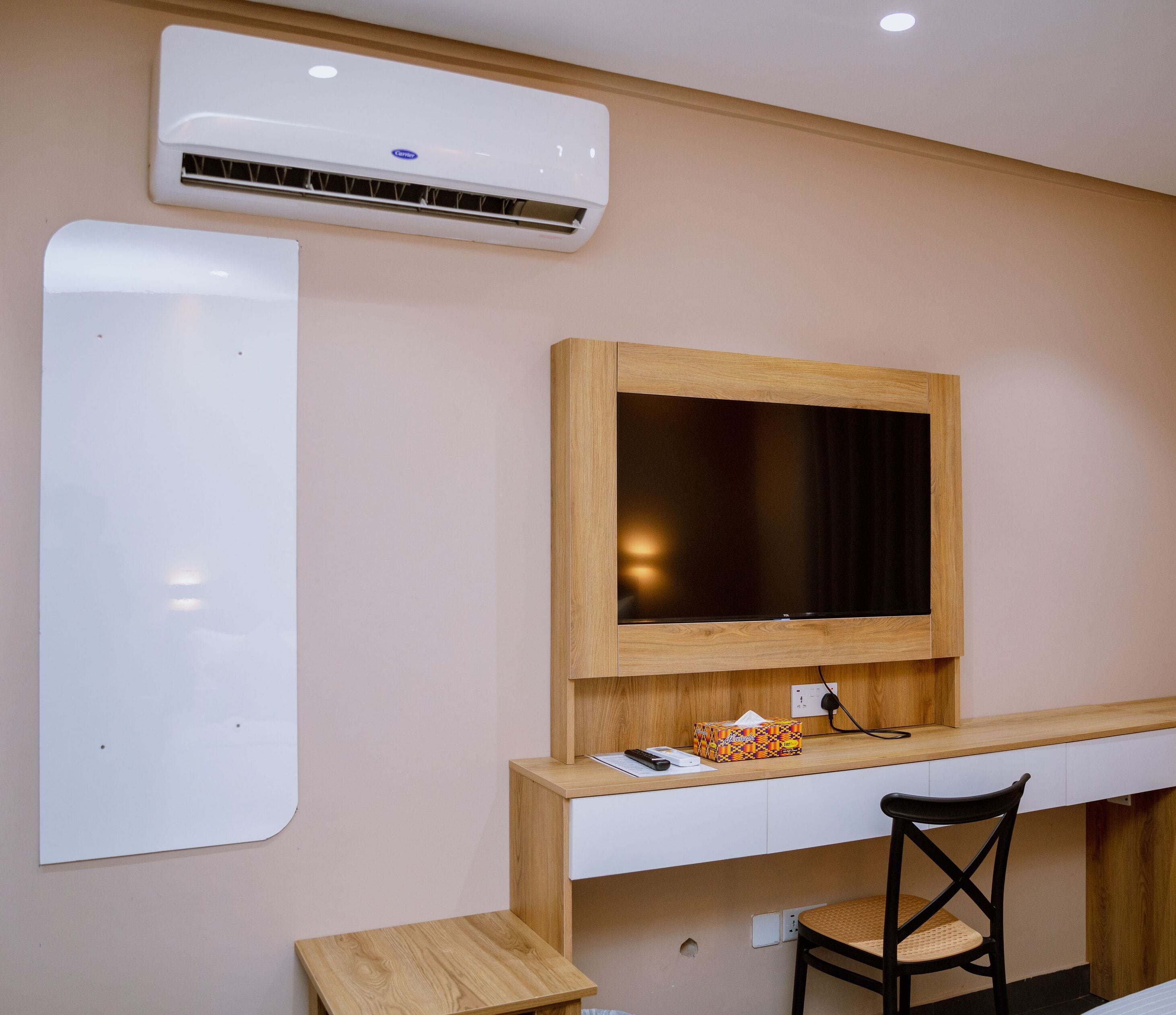 A modern room with a wooden desk, a black chair, a mounted TV, and an air conditioning unit.