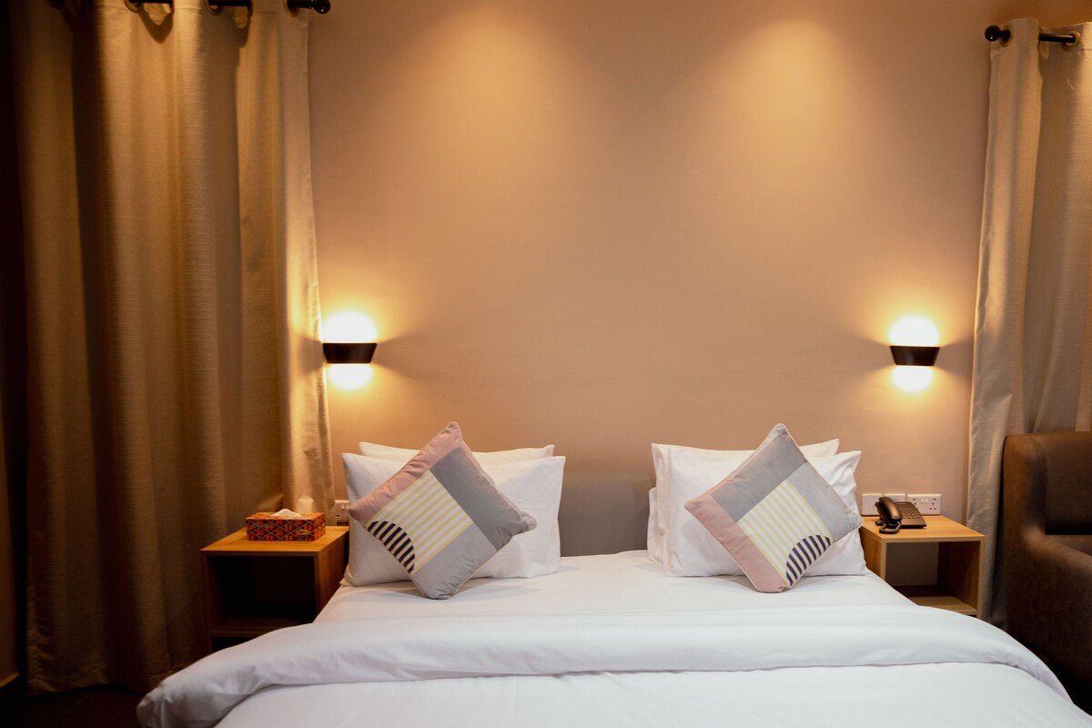 A hotel room with a large bed, two bedside tables with lamps, and a curtain.