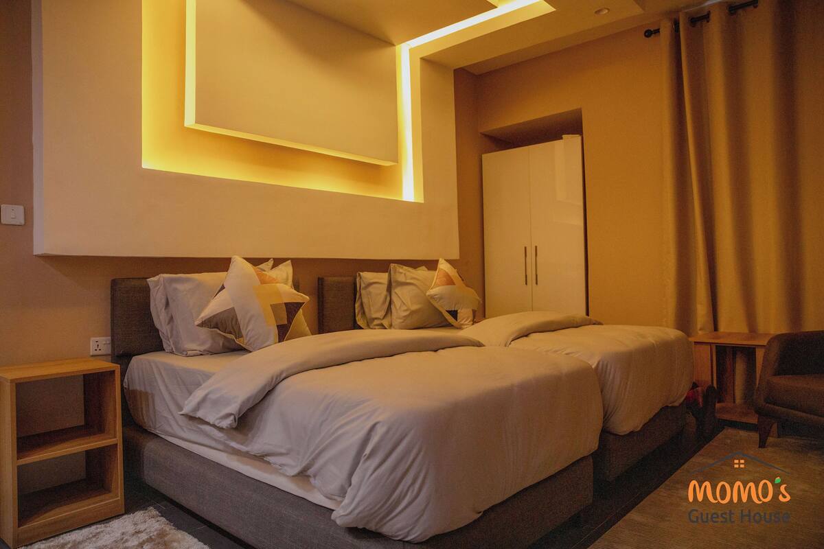 A modern hotel room with a double bed, bedside tables, a wardrobe, and a small seating area.