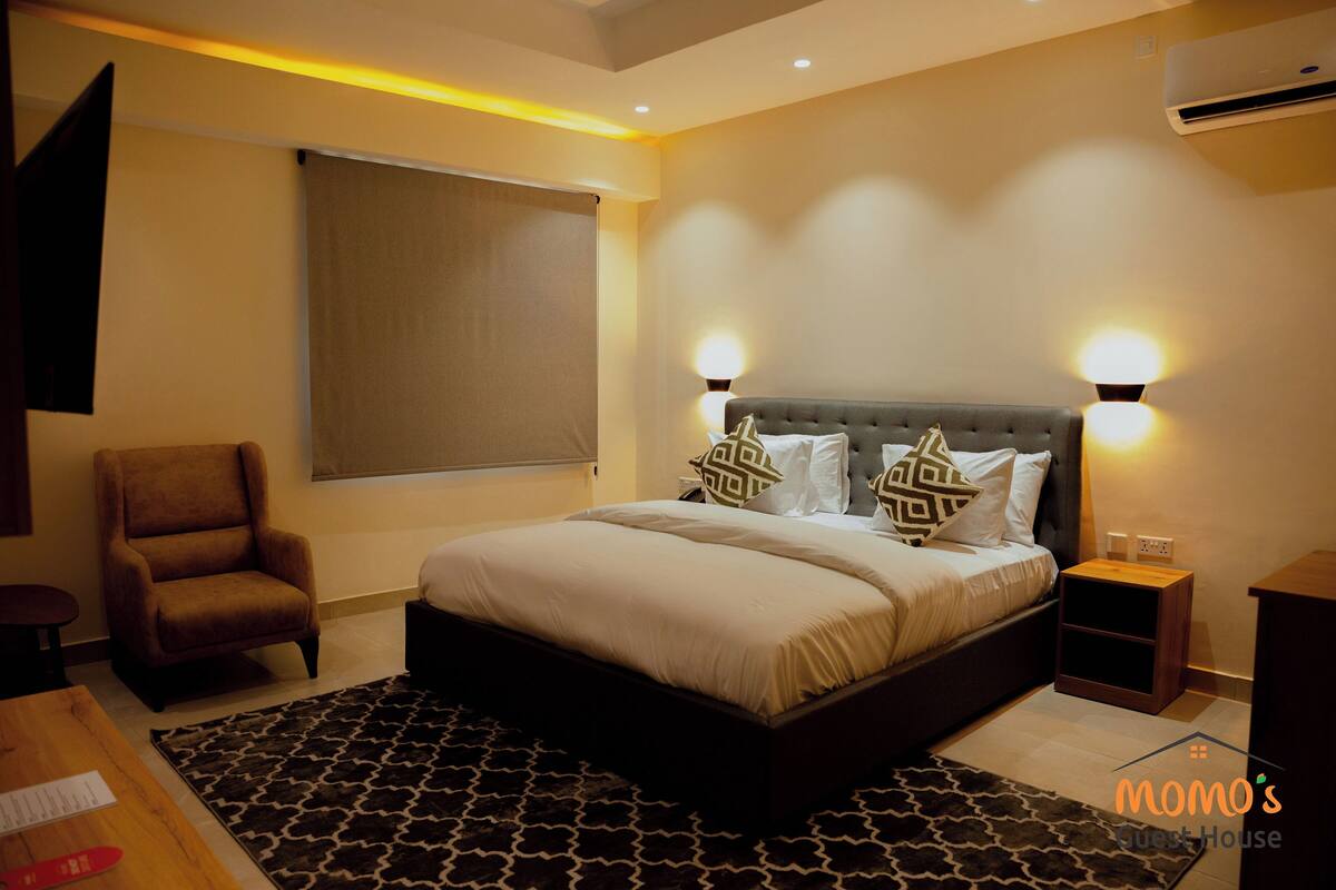 A modern bedroom with a large bed, a chair, a bedside table, and a wall-mounted TV.