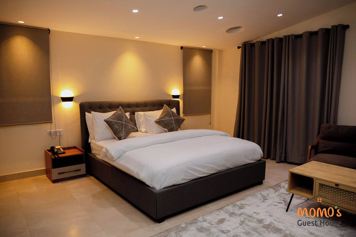 A modern bedroom with a large bed, bedside tables, a wooden coffee table, and a view of the outdoors.