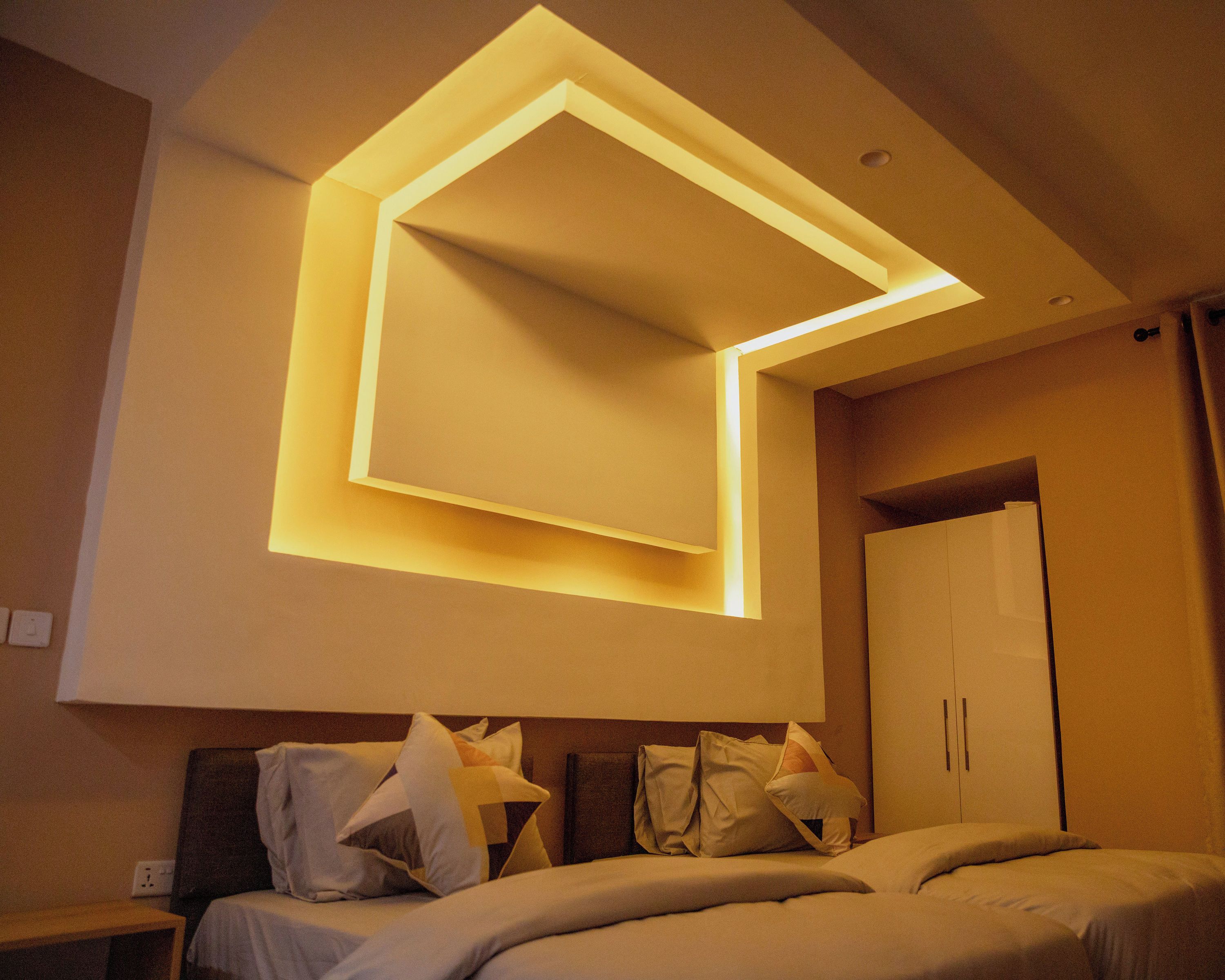 Habitación de hotel con cama, mesita de noche, armario y una lámpara de techo moderna.