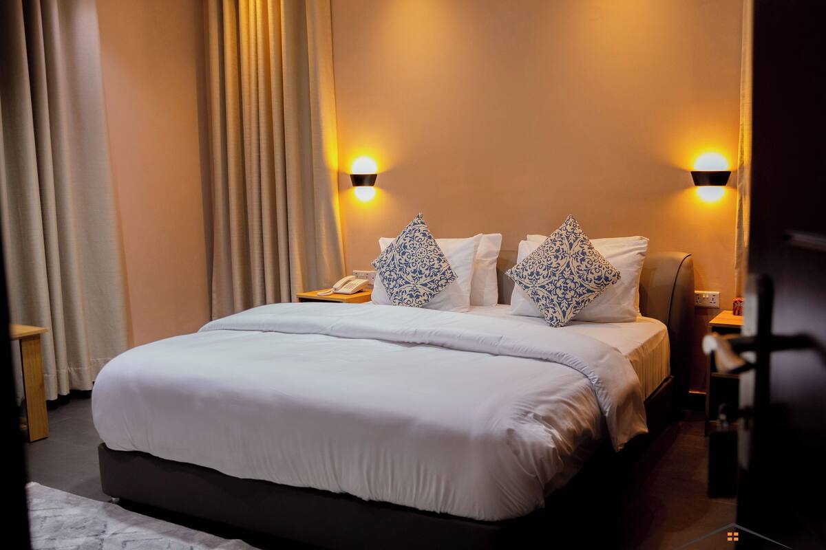 A hotel room with a large bed, two bedside lamps, a telephone, and a nightstand.