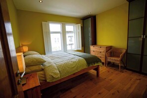 Um quarto com cama de madeira, cómoda, cadeira e guarda-roupa.