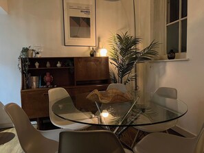 Ein moderner Essbereich mit einem Glastisch und Stühlen, einem Bücherregal und einem gerahmten Bild an der Wand.