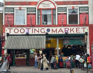 Fachada de un comercio con un gran letrero que dice 'TOOTING MARKET' y un letrero más pequeño arriba que indica '1930'.
