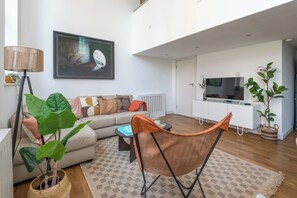 Ein modernes Wohnzimmer mit einem Sofa, einem Couchtisch, einem Sessel, einer Stehlampe, einem Gemälde, einem Fernseher und einer Topfpflanze.