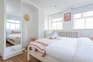Un dormitorio con cama, espejo, radiador y ventana.