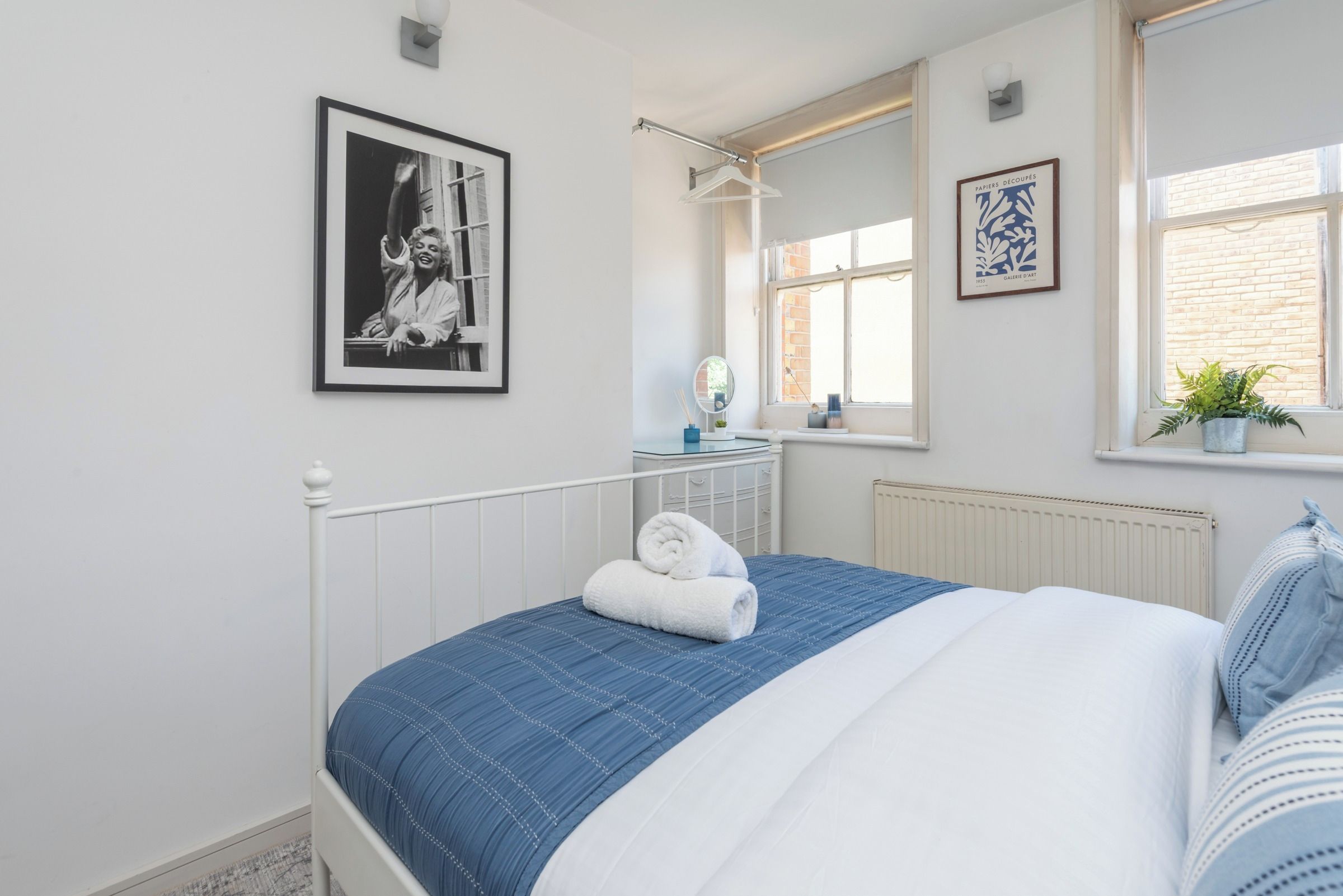 A bedroom with a bed, a dresser, a mirror, and two framed pictures on the wall.