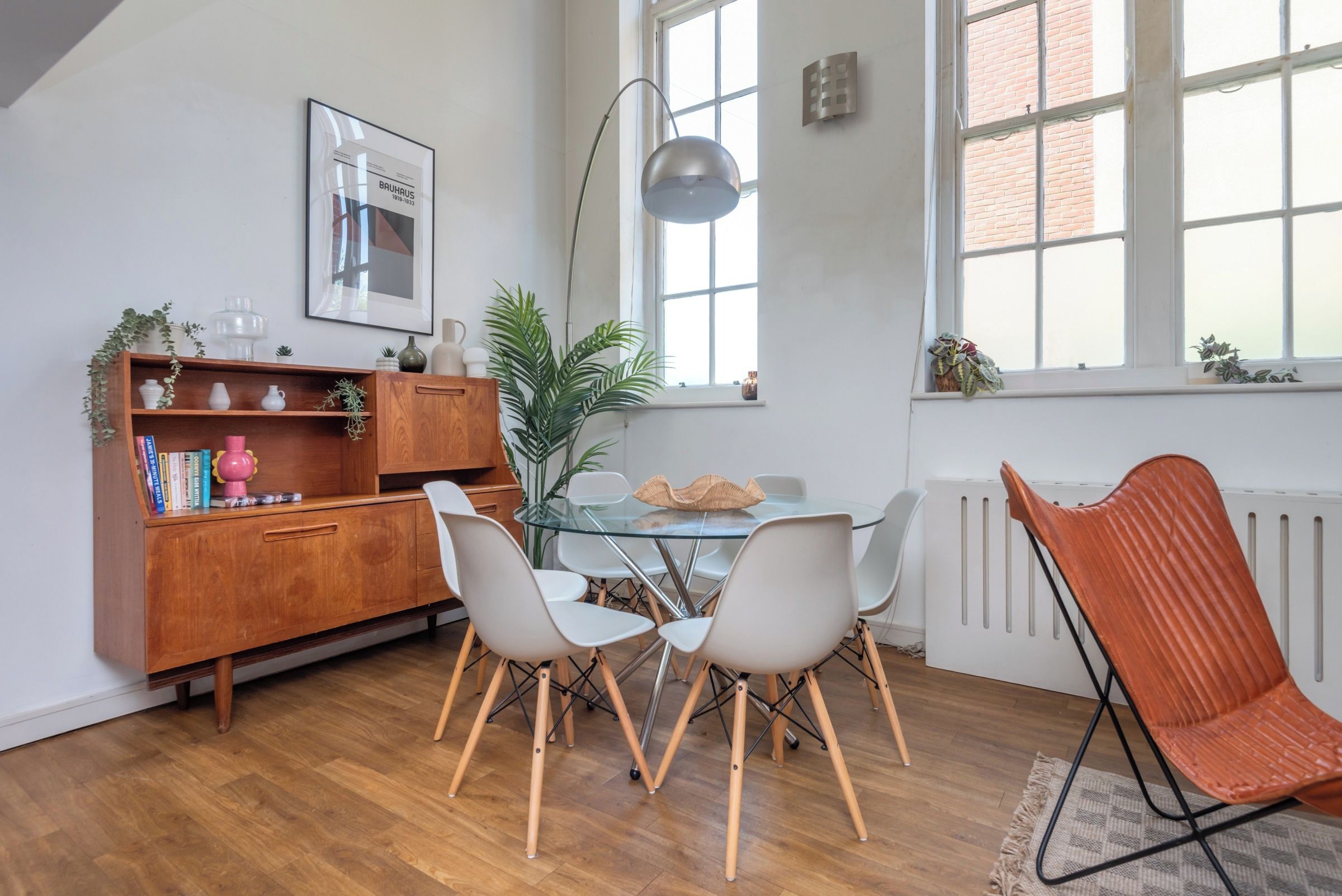 A dining area with a glass table, white chairs, a wooden cabinet, and a radiator.