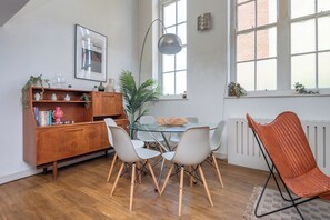 A dining area with a glass table, white chairs, a wooden cabinet, and a radiator. - Sunlit 3BDR Loft Near Tooting Broadway (Greater London)