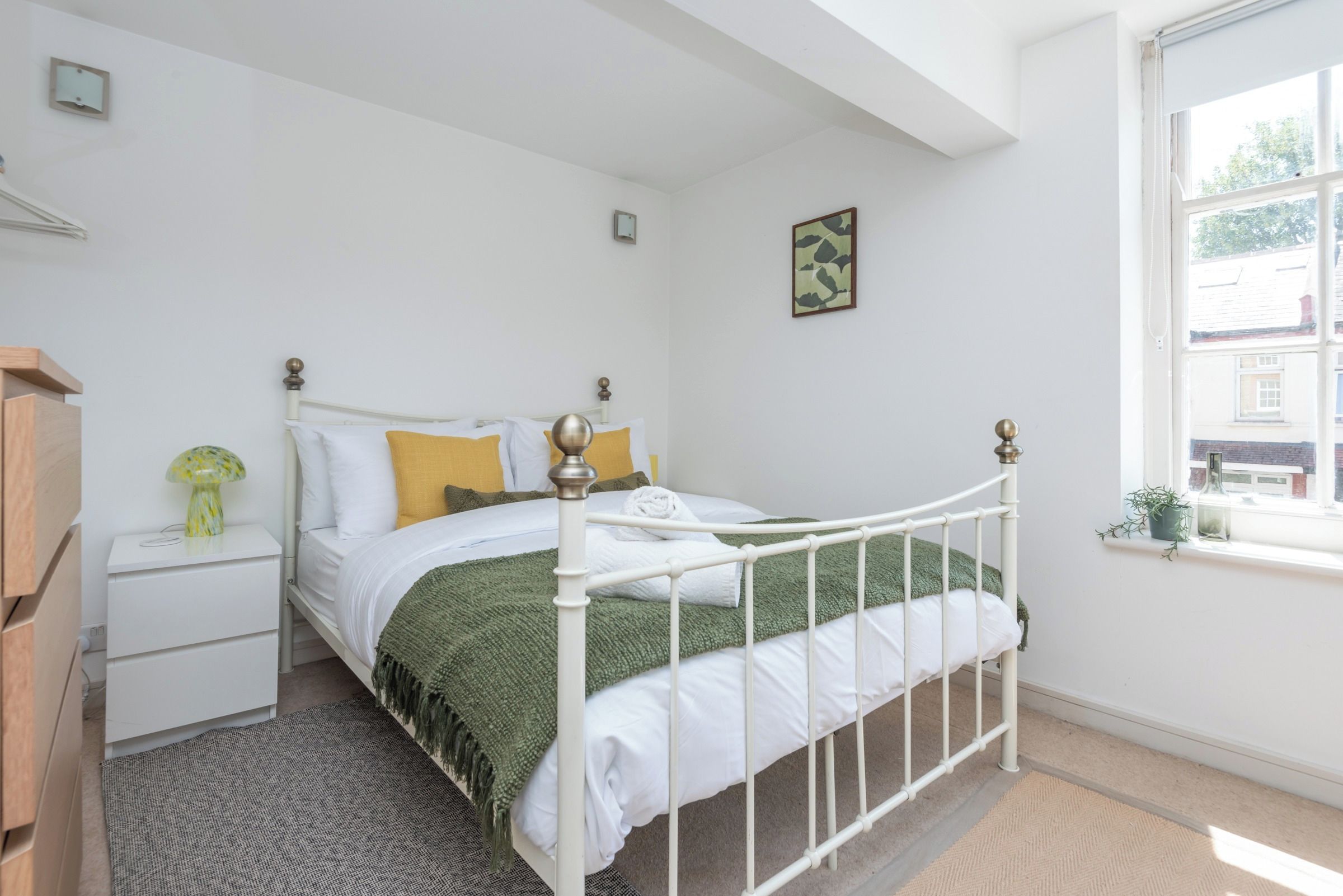 A bedroom with a white metal bed frame, a green throw blanket, and a white pillow.