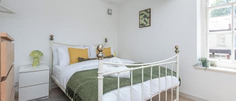 A bedroom with a white metal bed frame, a green throw blanket, and a white pillow.