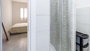 A bathroom with a glass shower enclosure, white tiled walls, and a visible trash bin. - Apartment in With Swimming Pool and sea View (Castelsardo)