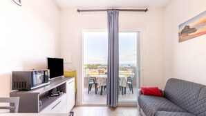 A room with a TV, a sofa, a balcony with a table and chairs, and a painting on the wall. - Apartment in With Swimming Pool and sea View (Castelsardo)