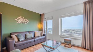 Una sala de estar moderna con un sofá de cuero marrón, una mesa de centro de vidrio y vista al mar a través de amplios ventanales.