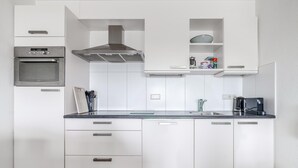 Una cocina moderna con armarios blancos, una campana extractora de acero inoxidable, horno integrado y cafetera.