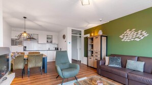 Una sala de estar moderna con un sofá de cuero marrón, una mesa de centro de vidrio y una zona de comedor con una mesa y sillas de madera.